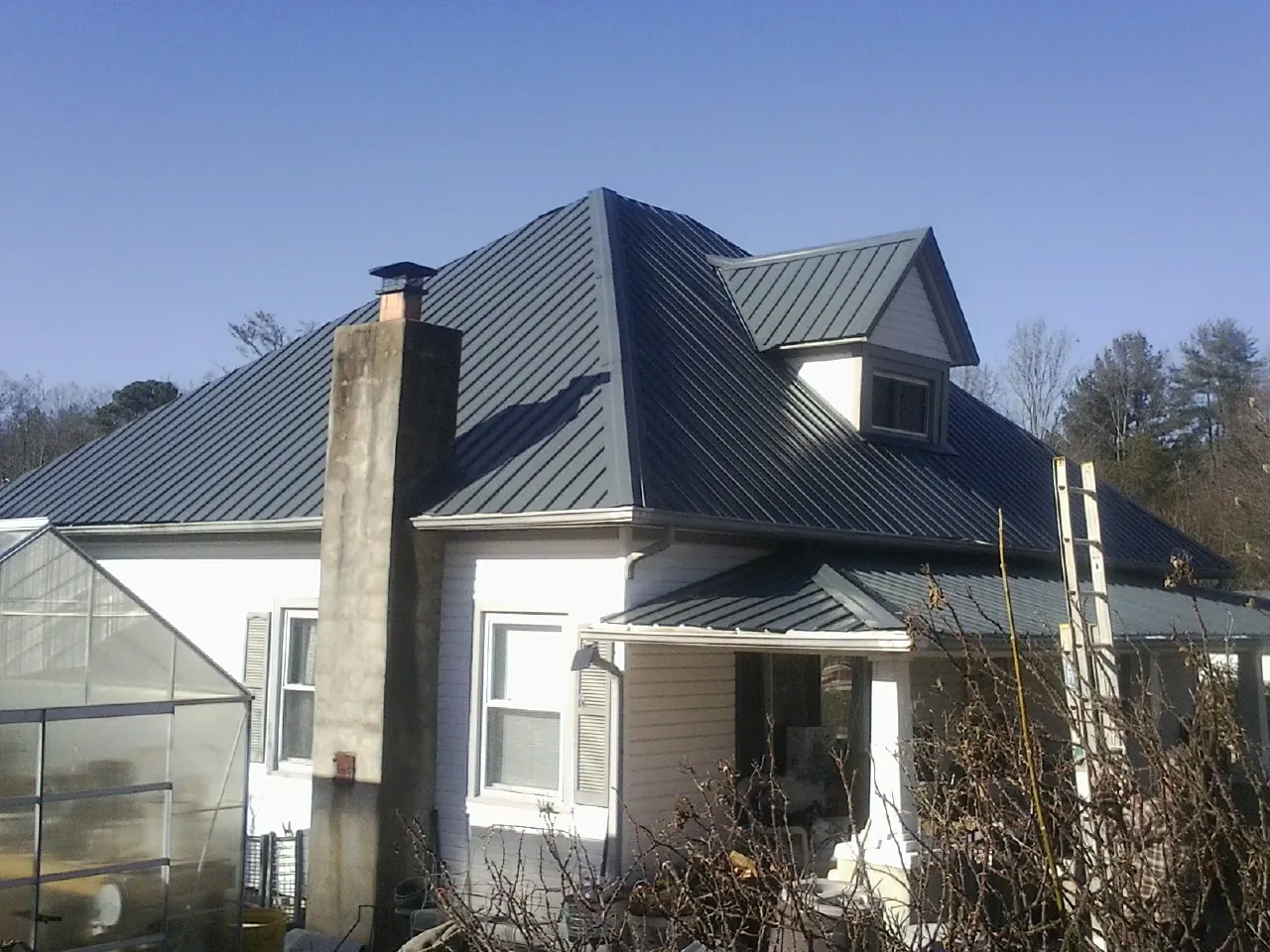 Dark blue standing seam metal roof on a white farmhouse with dormer — Slate & Tile Roof Repair by Roofing Brothers in Inkster