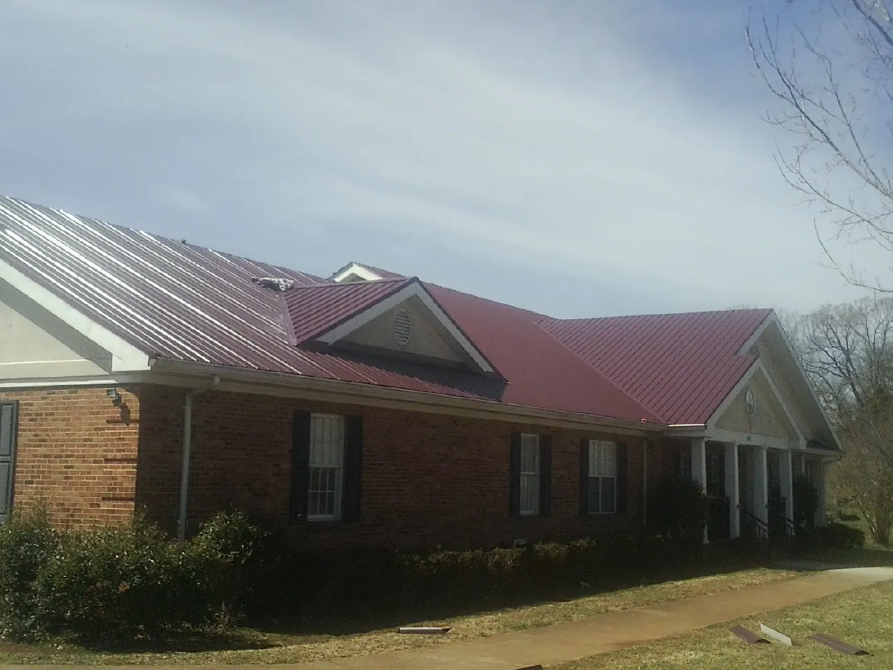 Red metal roof with gabled entries on a long brick building, from a Hail Damage Roof Repair job in Inkster