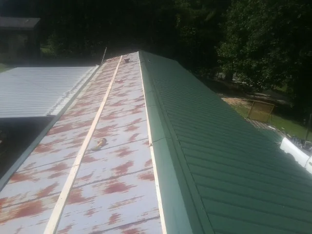 Old rusted panels beside newly installed green metal roofing — Wind Damage Roof Repair by Roofing Brothers in Inkster