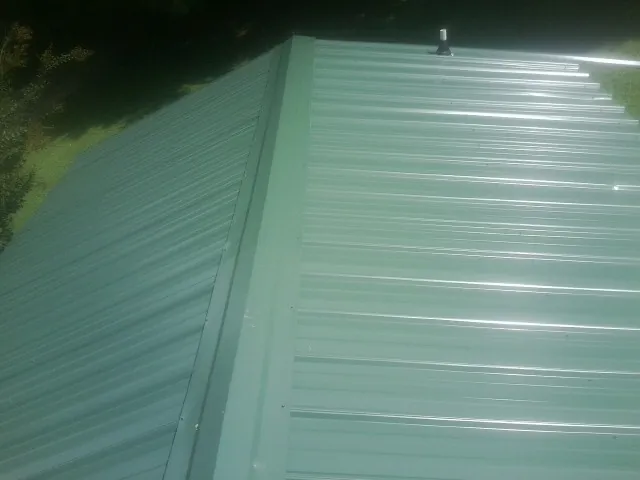 New green metal panels meeting at the ridge of a roof — Flat Roof Repair work by our crew in Inkster