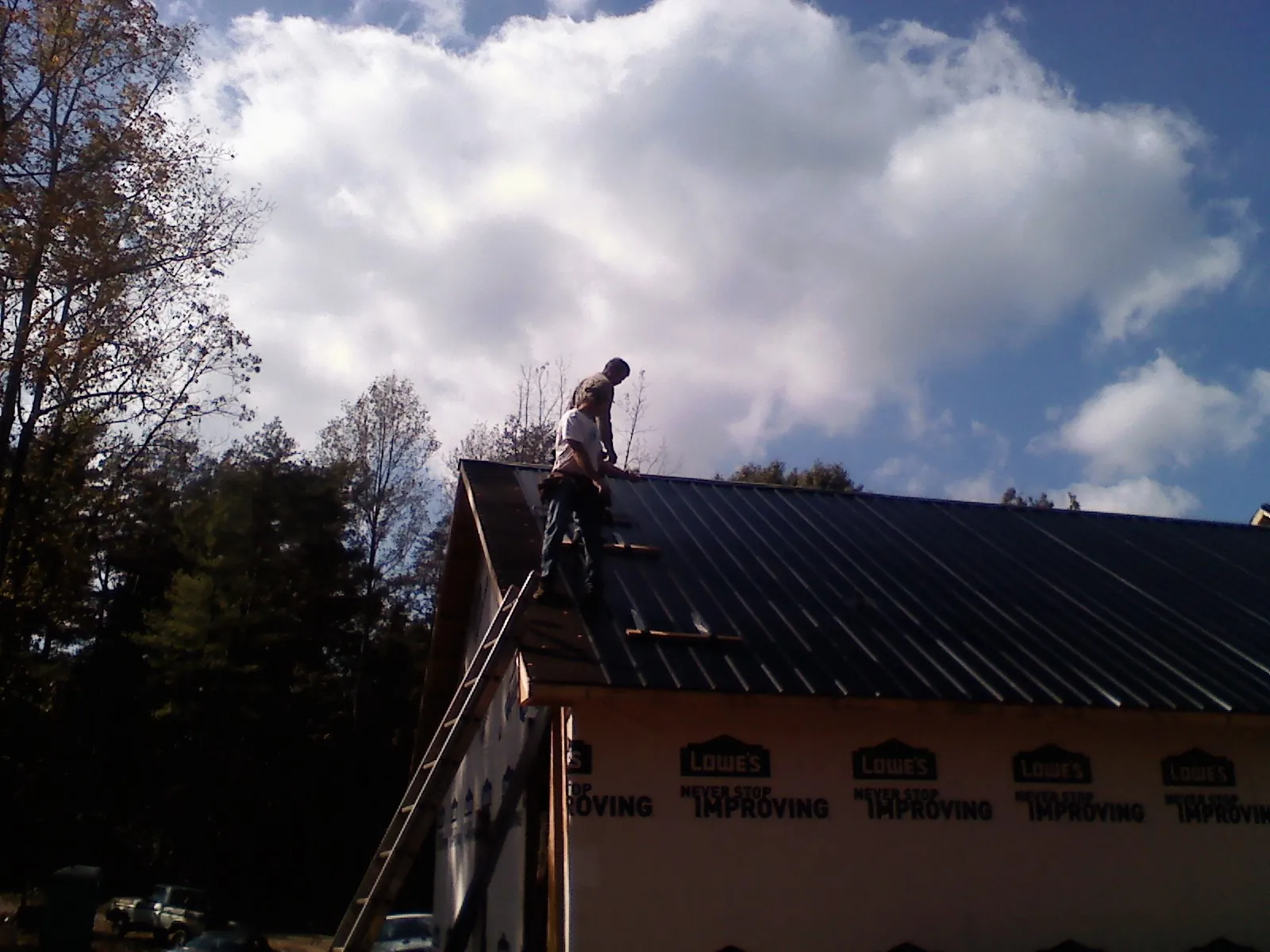 Roofer fastening dark metal panels high against a cloudy sky, from a Roof Inspection job in Inkster
