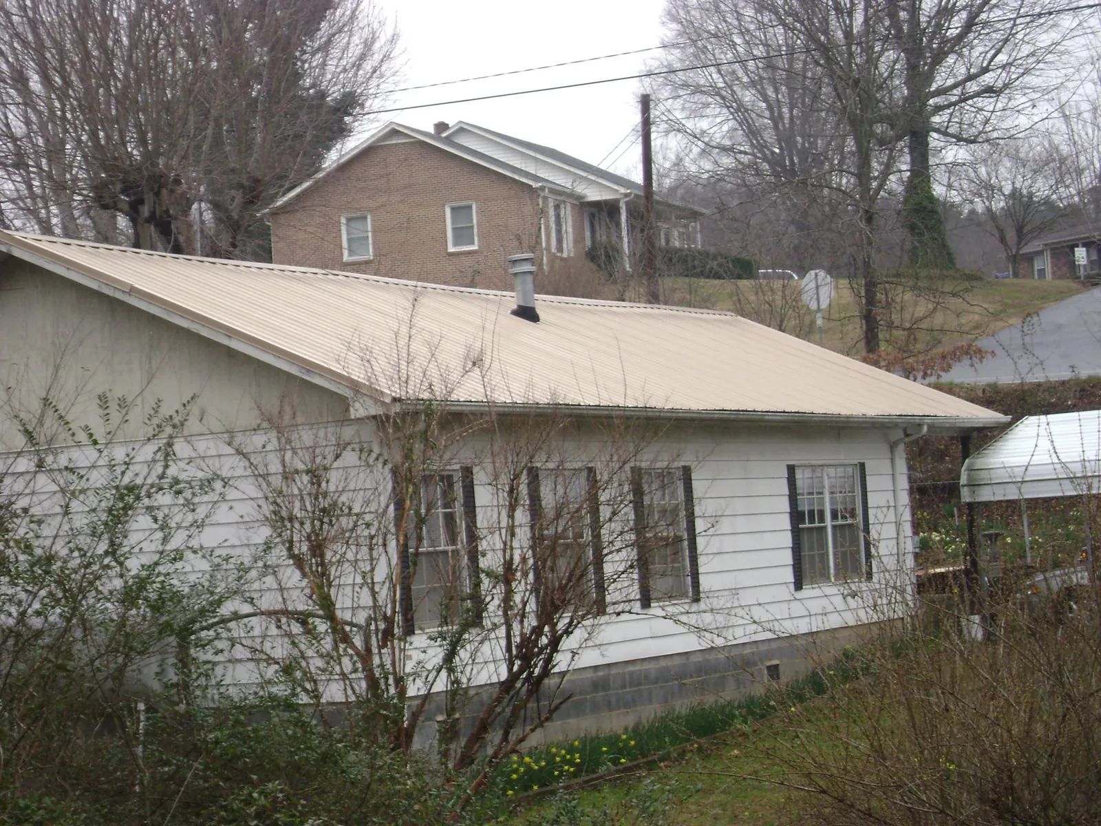 Tan metal roof on a white sided house set into a hillside — Commercial Roofing by Roofing Brothers in Inkster